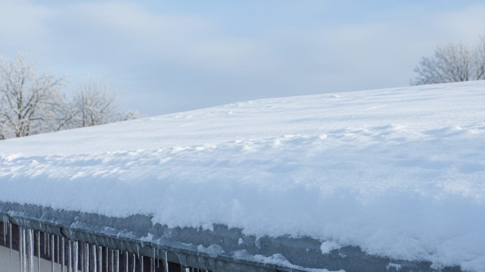 Lange Eiszapfen an einer Attikakante mit angesammeltem Eisring – Zeichen für Eisstau und unzureichende Dämmung.