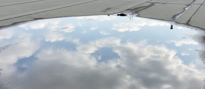 Stehende Wasserpfütze auf einem grauen Flachdach nach Regen.